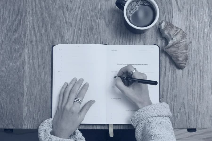 Hands writing in a notebook beside a laptop.