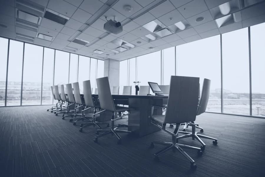 An empty boardroom with chairs drawn up to a long table, waiting for the people who will fill it.